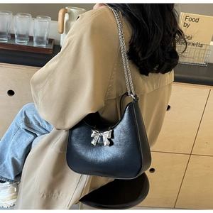 Detail of black faux leather underarm bag with silver bow accent and metal chain strap