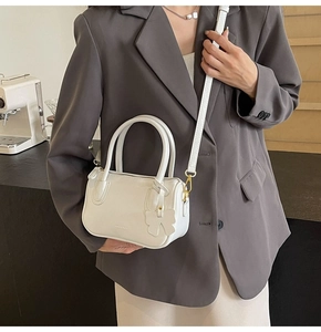 White faux leather mini Boston bag with gold hardware and bow charm detail shown on a model