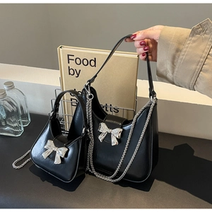 Detail showing glossy black leather crescent bag with silver bow accent and chain strap