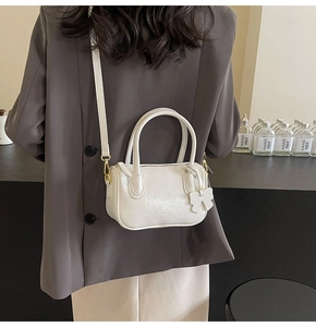 Detail of white PU leather crossbody bag with bow charm on a model in a grey suit