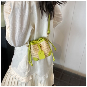 Model wearing a mini straw drawstring bucket bag with lime green leather accents and golden hardware