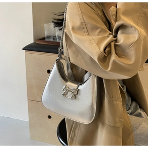 Detail of silver bow on metallic shoulder bag with shiny texture and metal chain strap