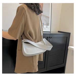Detail of grey crossbody bag featuring wide shoulder strap with round metal studs