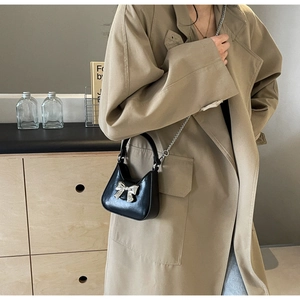 Model wearing a black bow chain bag over a tan coat showing actual product size