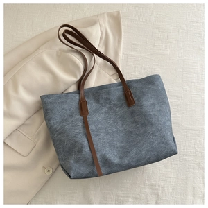 Borsa tote grigia in pelle scamosciata con manici marroni su sfondo blazer beige