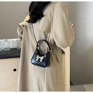 Mini black leather crossbody bag with silver bow detail worn with a trench coat