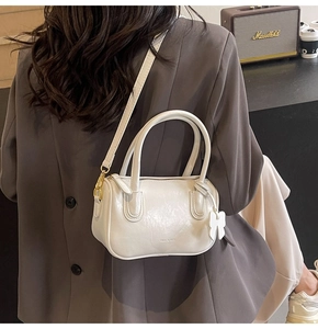 Close-up of a white cylindrical PU leather handbag with a bow charm and brand logo