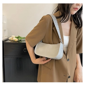 Close-up of stylish grey rivet shoulder bag with wide grommet strap on model