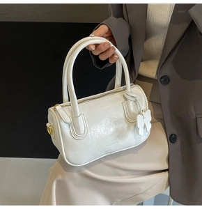 Macro shot of white cylindrical Boston bag in glossy PU leather with gold hardware