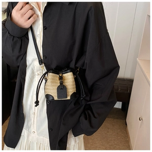 Detail of a small straw bucket bag with black leather trim and vintage metal buckles