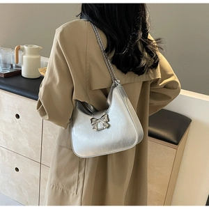 Silver metallic bow bag detail with chain strap shown on model in cafe setting