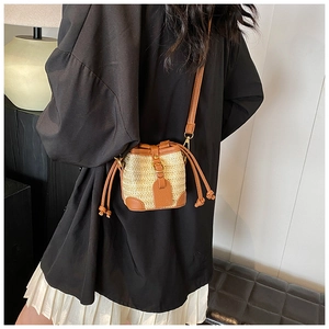Mini straw bucket bag with brown leather trim shown worn crossbody with a white pleated skirt