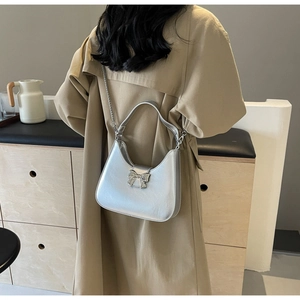 Detail view of silver crescent hobo bag with metal bow buckle on beige trench coat
