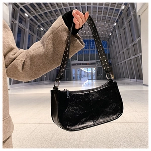Detail of black patent leather underarm bag featuring silver rivets on a wide strap