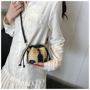 Detailed close-up of straw bucket bag featuring black leather trim and drawstring closure