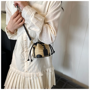 Detail view of mini straw bucket bag with black leather trim and crossbody strap on model