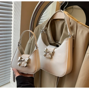 Comparison of two white crescent bags with silver bow accents on a trench coat background