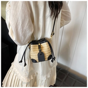 Mini beige straw bucket bag with black leather trim and drawstring shown on female model