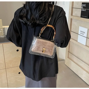 Detail of transparent PVC handbag with bamboo handle and woven inner pouch on shoulder