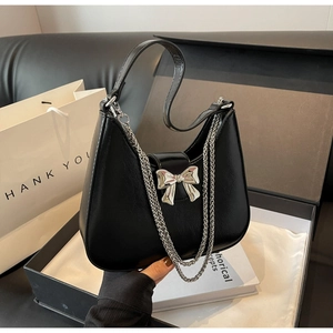 Detailed view of black leather handbag featuring a large silver bow buckle and dual chains