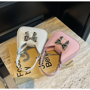 Detail view of white and pink bow handbags with silver chain straps on marble surface