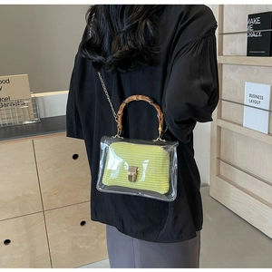 Detail of trendy clear PVC bag featuring a bamboo handle and bright green woven interior
