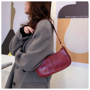 Close-up of stylish burgundy baguette bag with glossy texture and shoulder strap