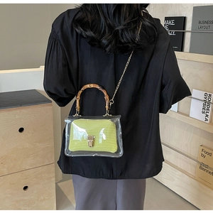 Detail of transparent PVC crossbody bag with bamboo handle and green woven pouch worn by model