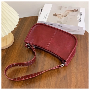 Detail of burgundy textured leather bag featuring a wide strap with silver metal rivets