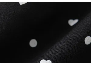 Detail view of black knit fabric featuring white polka dots and heart patterns