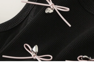 Macro detail of black ribbed fabric with pink bows and silver heart pendants on girl's dress