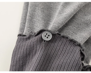 Detail van grijs gebreid vest met geribbelde textuur, decoratieve ruches en knoop