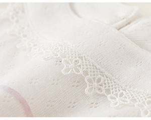 Close-up of white knitted baby top featuring intricate crochet lace trim and mesh texture