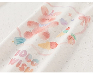 Macro view of white pointelle knit fabric featuring watercolor rabbit and fruit prints