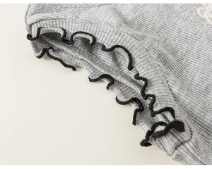 Detailed view of grey knitted hem with ruffled edges and black contrast stitching