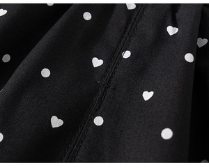 Close-up of black cotton fabric with white polka dots and heart patterns showing neat stitching