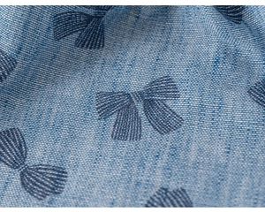 Close-up of light blue cotton fabric with detailed dark blue bow tie patterns and textures