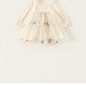 Détail de la jupe en tulle multicouche avec des pompons colorés sur une robe beige
