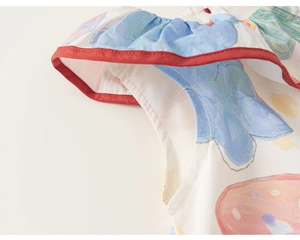 Detail eines Baby Mädchen Baumwollkleids mit blauem Blumendruck und rotem Rüschensaum