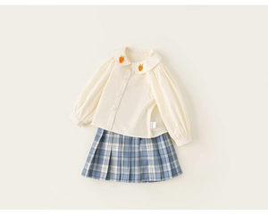 Detalle de camisa de niña con bordado de zanahoria y falda de cuadros plisada en estilo flat lay