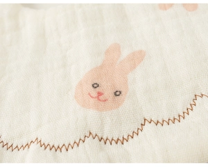 Close-up of muslin cotton baby bib featuring pink rabbit print and wavy stitched edges