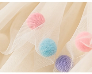 Détail du tissu en tulle blanc avec pompons colorés et texture de maille légère