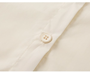 Detalle de una tapeta de camisa de algodón blanco crema con costuras limpias y botón de cuatro orificios