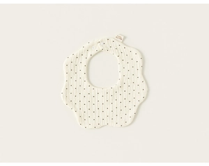 Detail of baby cotton bib with wave edges and black polka dots on beige muslin fabric
