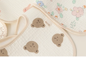 Detailed close-up of soft cotton baby bibs featuring bear and floral prints with fine texture