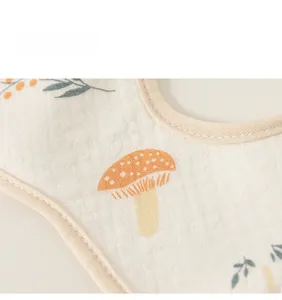 Close-up of cotton baby bib with orange mushroom print and soft gauze fabric texture