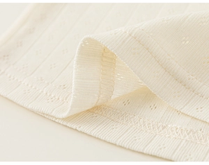 Close-up of cream knit fabric with pointelle heart patterns and ribbed edge detail