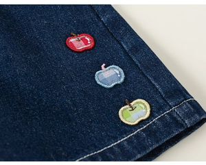 Gros plan de broderies pommes mignonnes sur denim bleu foncé avec coutures nettes