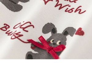 Detail of white knit fabric with gray bunny print, text and red 3D ribbon bow ornament
