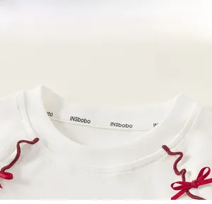 Close-up of white ribbed cotton round neck with a decorative red bow on the shoulder